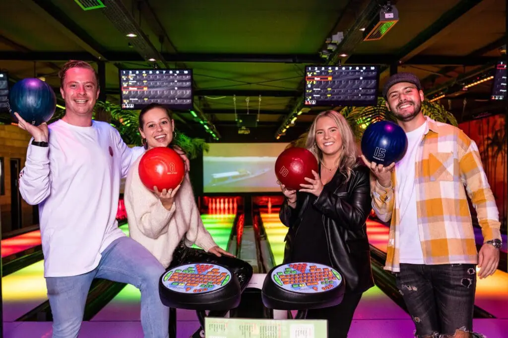 4 mensen met bowlingballen op een bowlingbaan