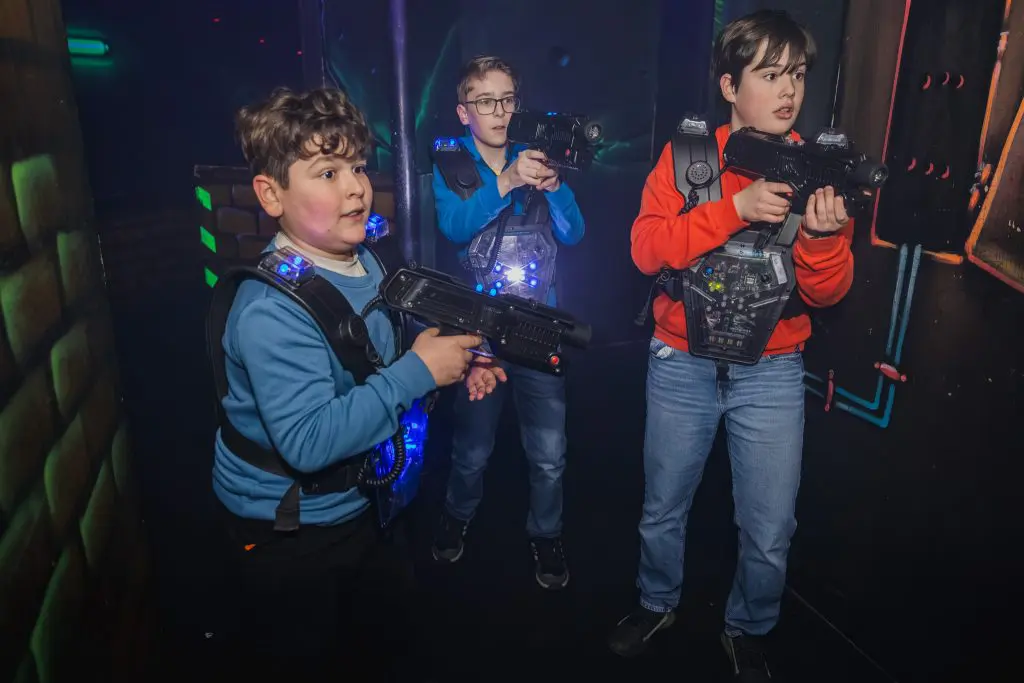 Drie jongens in lasergame area met lasergame guns en vesten aan